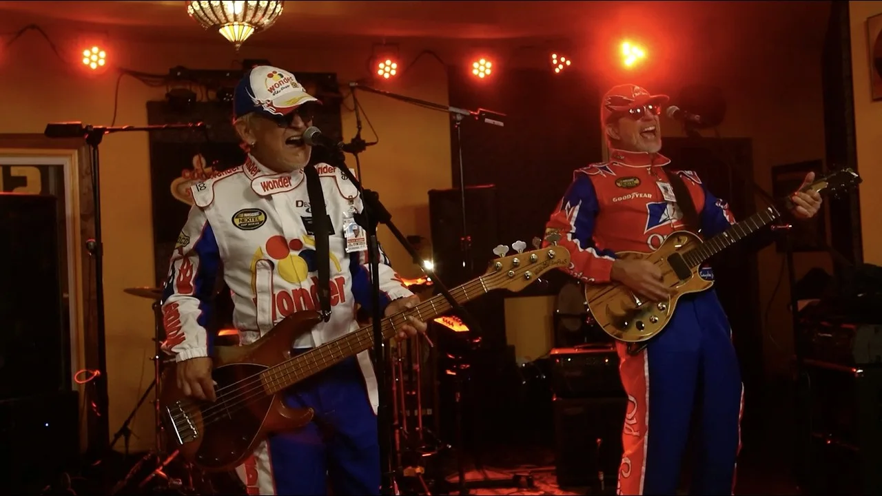 Rik and Bob of Ricky Bobby Music on stage in race suits
